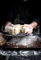 male hands breaking open baked bread in half over black wooden t