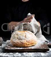 baked round bread on a board behind the cook in black clothes