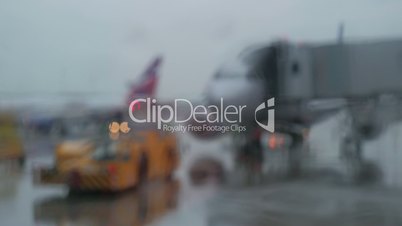 Tow tractor and aircraft, view on rainy day through the terminal window