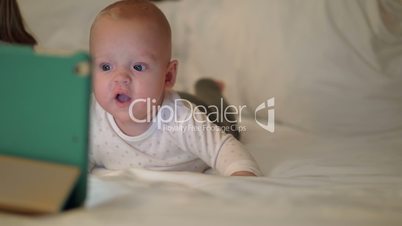 Cute baby girl lying on a bed and watching on tablet screen