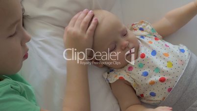 Boy lying on a bed with his baby sister and stroking on her head