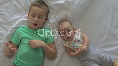 Boy and baby girl siblings on bed at home