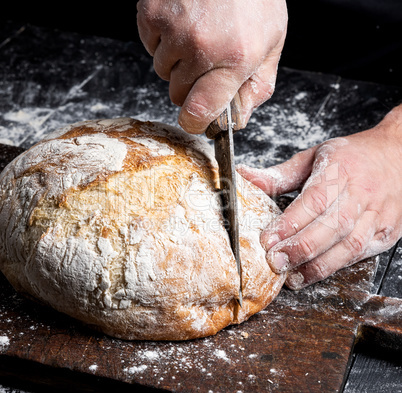 male hands cut a knife round baked bread male hands cut a knife round baked bread