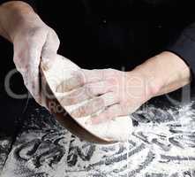 man's hands knead white wheat flour dough on black wooden backgr