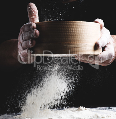 round wooden sieve with flour in male hands, the chef sifts whit