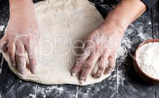 men's hands knead a round piece of dough