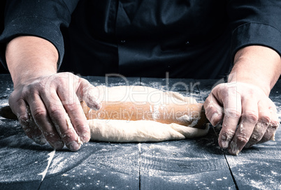 chef in a black tunic rolls a dough for a round pizza