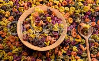 multicolored spiral raw pasta fusilli in a wooden bowl