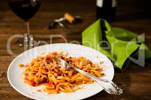 Half-eaten tagliatelle pasta with bolognese ragu and red wine