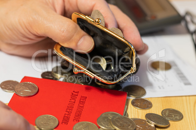 Hand pensioner, glasses, calculator and wallet with coins on the surface of the table. Translation of the inscription: "pensioner's Certificate"