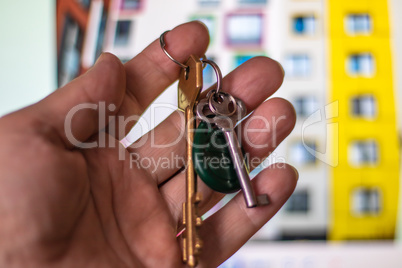 Close-up Photo of a man's hand holding the keys to a new house on the background of a modern residential building