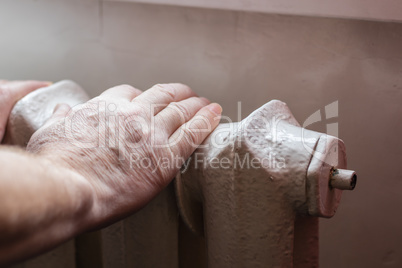 An elderly man warms his hands on the Central heating battery