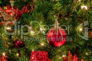 Red and green ornaments on a Christmas tree with white lights