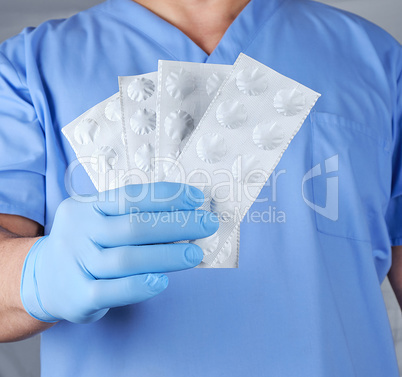 doctor in blue latex gloves holds pills in white paper packaging