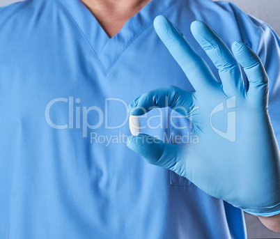 doctor in blue latex gloves holding a white pill