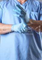 doctor in a blue uniform puts on sterile latex gloves