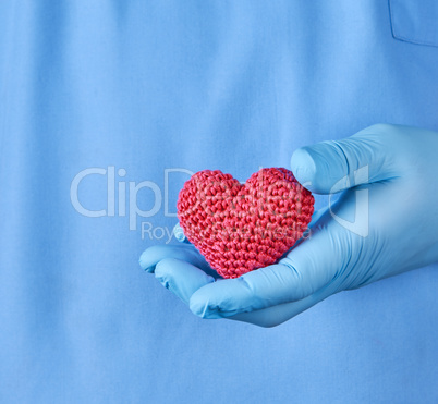 doctor with blue latex gloves holding a red heart