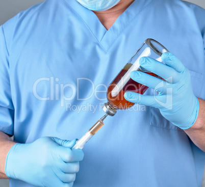 doctor in blue uniform holds a syringe and a glass bottle with