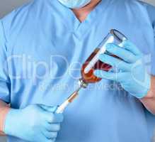 doctor in blue uniform holds a syringe and a glass bottle with