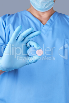 doctor in blue latex gloves holding a large round pill