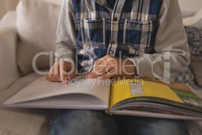Mid section of boy reading a story book in living room