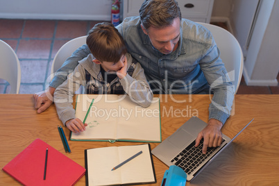 Father helping his son with his homework while using laptop