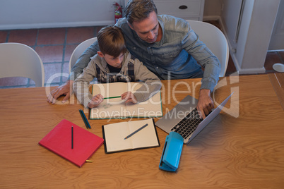 Father helping his son with his homework while using laptop