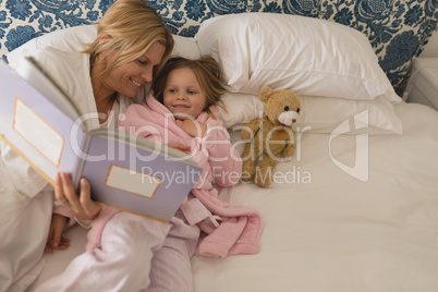 Mother with her daughter reading storybook in bedroom