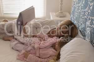 Mother with her daughter reading storybook in bedroom