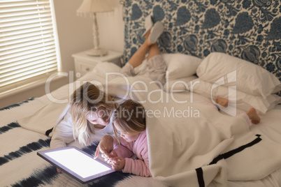 Mother and daughter using digital tablet in bedroom