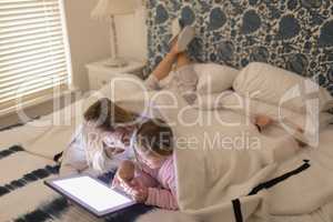 Mother and daughter using digital tablet in bedroom