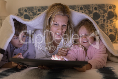 Mother with her children using digital tablet under blanket in bedroom