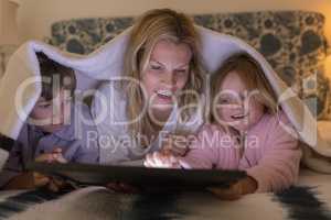 Mother with her children using digital tablet under blanket in bedroom