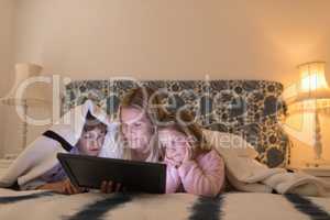Mother with her children using digital tablet under blanket in bedroom