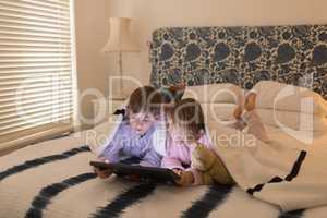 Siblings using digital tablet under blanket in bedroom