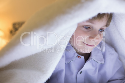 Boy relaxing under blanket in bedroom at home