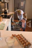 Mother with her daughter removing muffin cakes from oven in kitchen