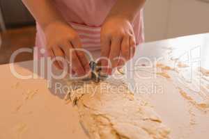 Mid section of girl using cookie cutter in kitchen