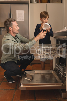 Father and son placing bowl in dishwasher in the kitchen