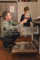 Father and son placing bowl in dishwasher in the kitchen