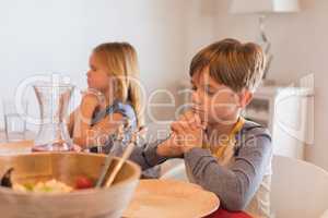 Siblings praying before having food on dining table
