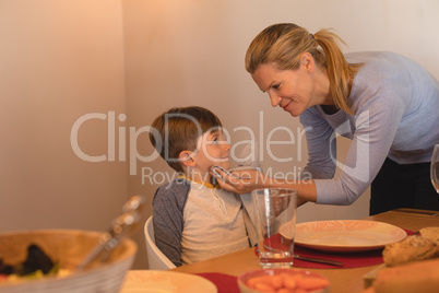 Mother wiping sons mouth with a napkin on dining table