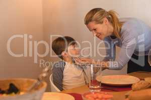 Mother wiping sons mouth with a napkin on dining table