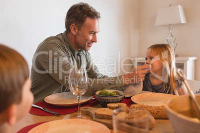 Father wiping daughters mouth with a napkin on dining table