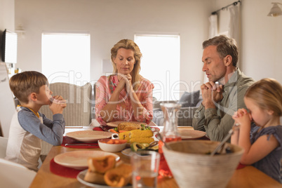 Family praying before having food on dining table