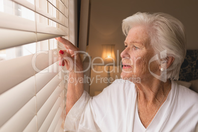 Senior woman looking through window blinds