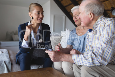Female doctor and senior couple discussing over clipboard