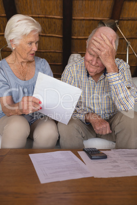 Worried senior couple discussing over medical bills in living room