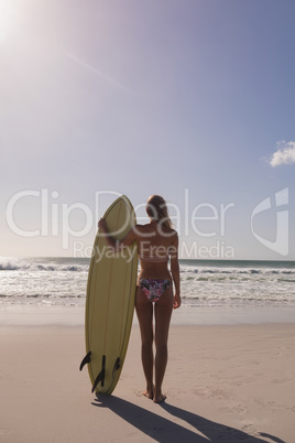Female surfer standing with surfboard at beach