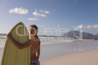 Female surfer standing with surfboard at beach